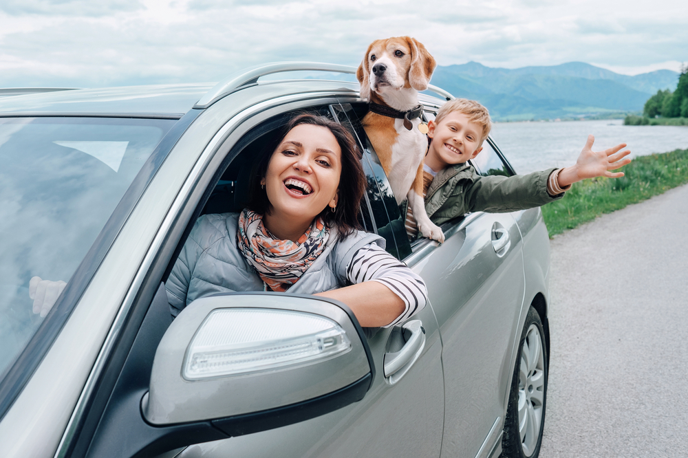 A happy mother with her son and dog waving from the window of a car